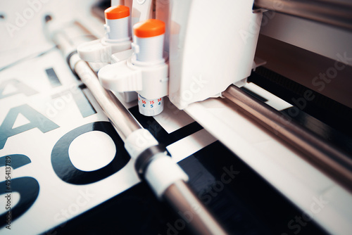 side view on tool head of cutting plotter equiped with adjustable blades. making of adhesive lettering from black vinyl foil in bright light. high contrast. selective focus. advertising concept