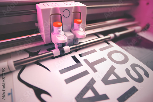 cutting plotter equiped with two adjustable blades makes adhesive lettering from black vinyl foil in energetic pink light. selective focus. advertising and political movement concept photo