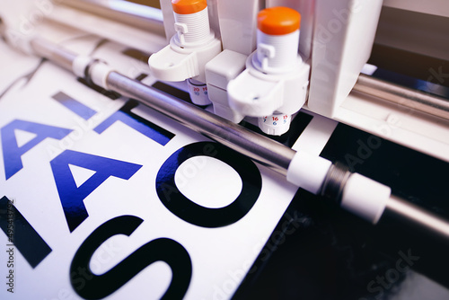 Fotografie tool head of cutting plotter equiped with two adjustable blades makes adhesive lettering from black vinyl foil in bright light