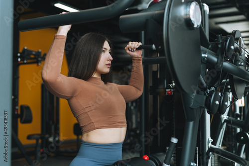 Young fitness brunette woman training for back muscles equipment at gym