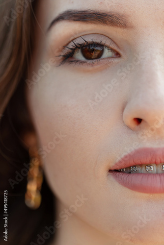 Closeup portrait of beautiful Caucasian teenager woman model with brown eyes, clean skin and dental brackets looks at the camera. Half a woman's face