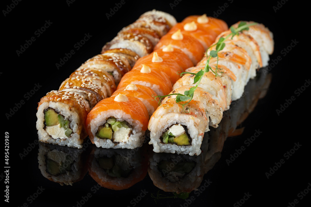 Traditional delicious fresh sushi roll set on a black background with reflection. Sushi roll with rice, nori, cream cheese, tobiko caviar, avocado. Sushi menu. Japanese kitchen. Asian food Traditional delicious fresh sushi roll set on a black background with reflection. Sushi roll with rice, nori, cream cheese, tobiko caviar, avocado. Sushi menu. Japanese kitchen. Asian food