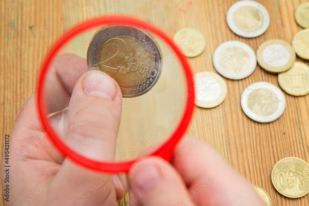 Fototapeta premium Euro coins magnified by hand magnifier. The young man holds a magnifying glass over the coins. The concept of inflation, poverty, economic crisis.