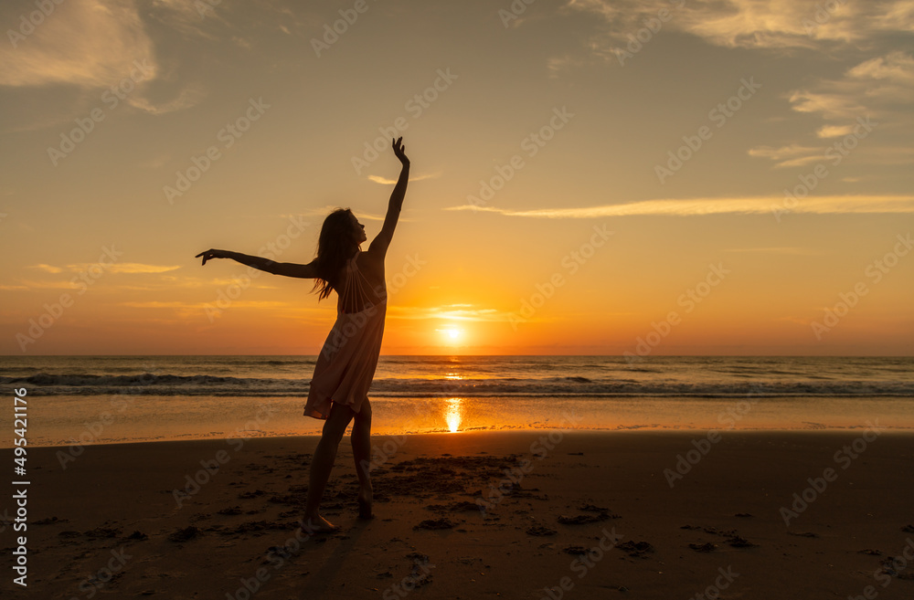 Young carefree female dancing on beach at sunset