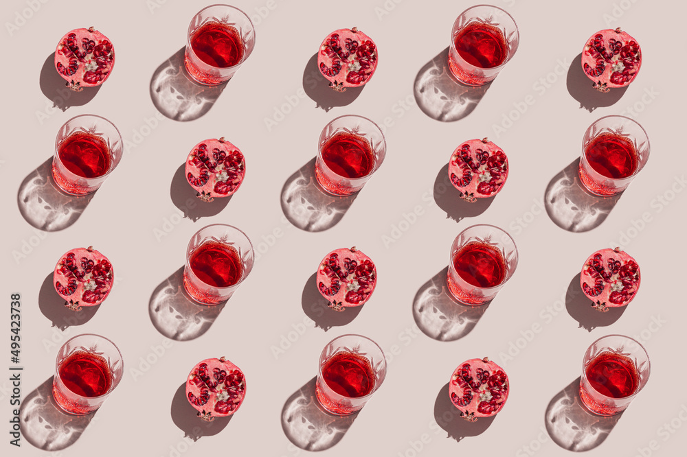 Creative pattern made of a half of pomegranate and glass with juice or red wine on pastel beige background. Summer fruit and refreshment  concept. Minimal style. Sunlit flat lay. Top view