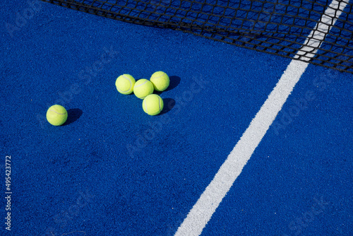 five paddle tennis balls and the net of a blue paddle tennis court, selective focus © VicVaz