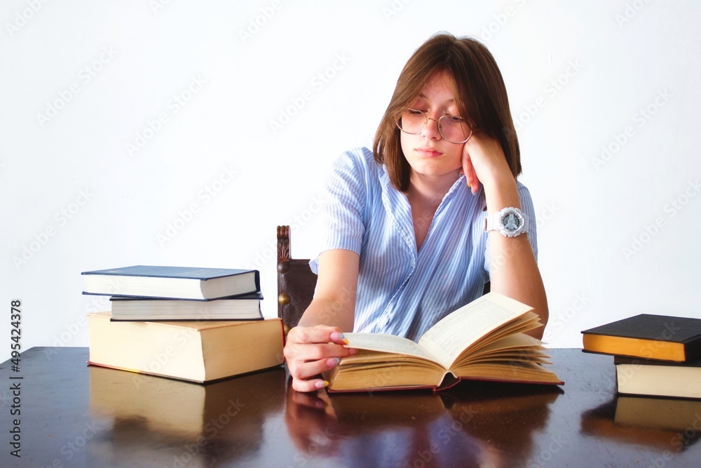 A white caucasian young teen student sitting at a table reading books looking bored A white caucasian young teen student sitting at a table reading books looking bored