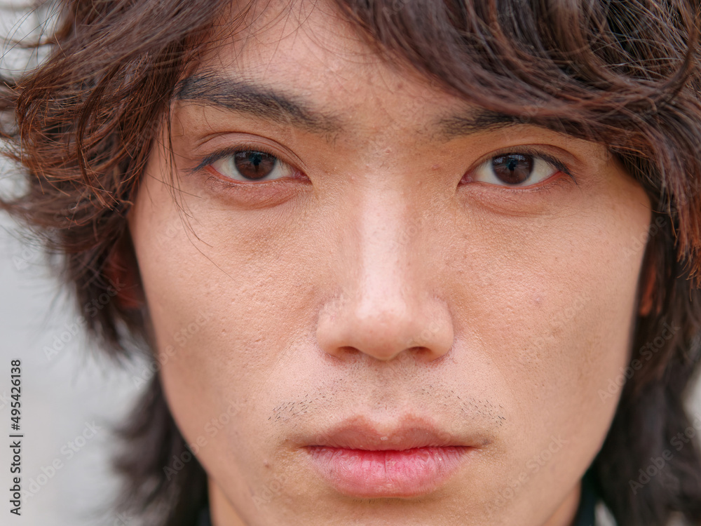 Fototapeta premium Portrait of handsome Chinese young man in black looking at camera with gray wall background, front view of confident young man, close up view head shot.