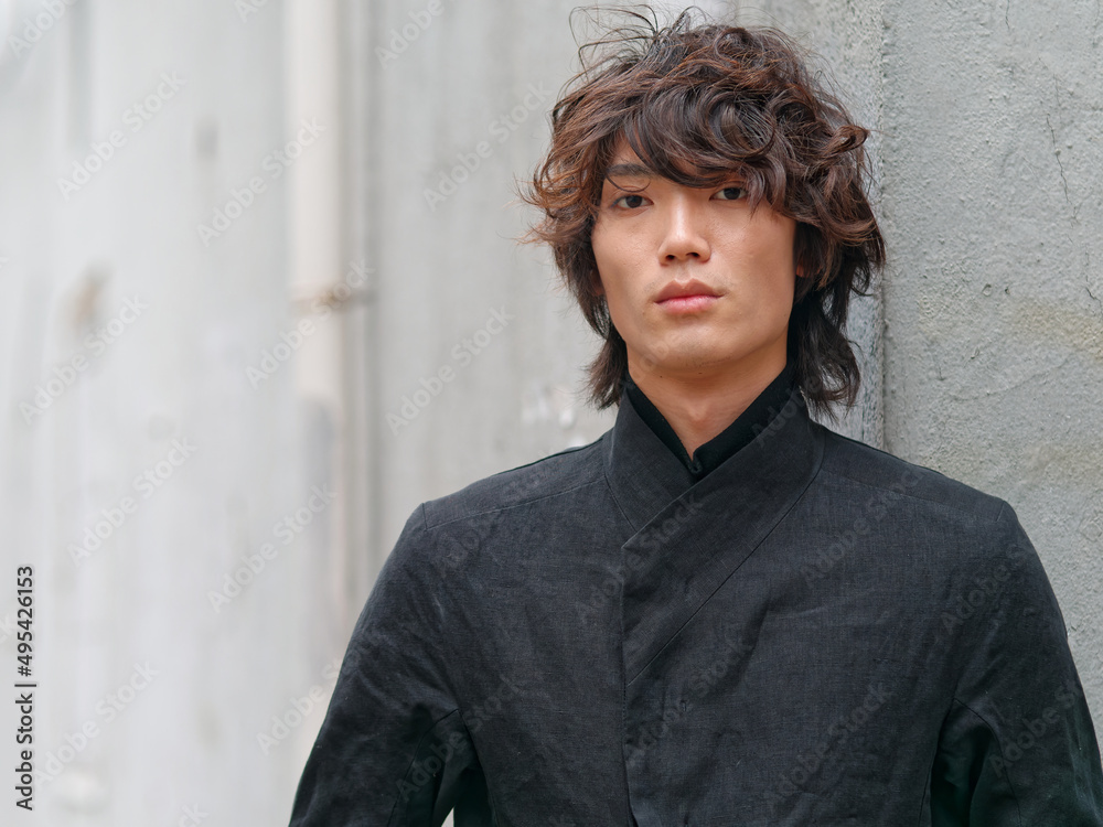 Portrait of handsome Chinese young man in black looking at camera with gray wall background, front view of confident young man. Portrait of handsome Chinese young man in black looking at camera with gray wall background, front view of confident young man.