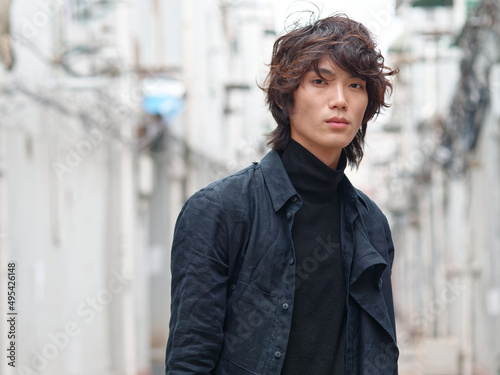 Portrait of handsome Chinese young man in black looking at camera with narrow street background, front view of confident young man.
