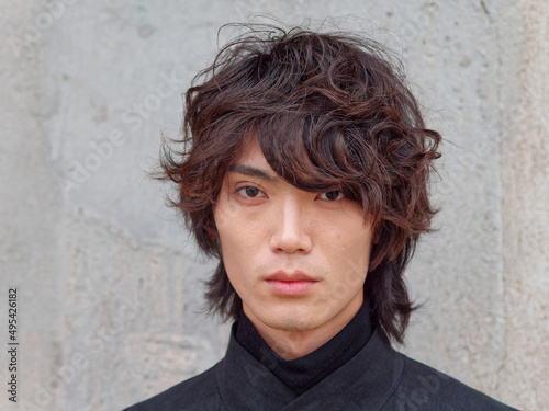 Portrait of handsome Chinese young man in black looking at camera with gray wall background, front view of confident young man, close up view head shot.