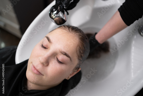 young woman, lies in a salon, washes her hair in a hairdressing salon by a stylist. Handsome client relaxing while hairdresser massaging and washing hair with water and shampoo