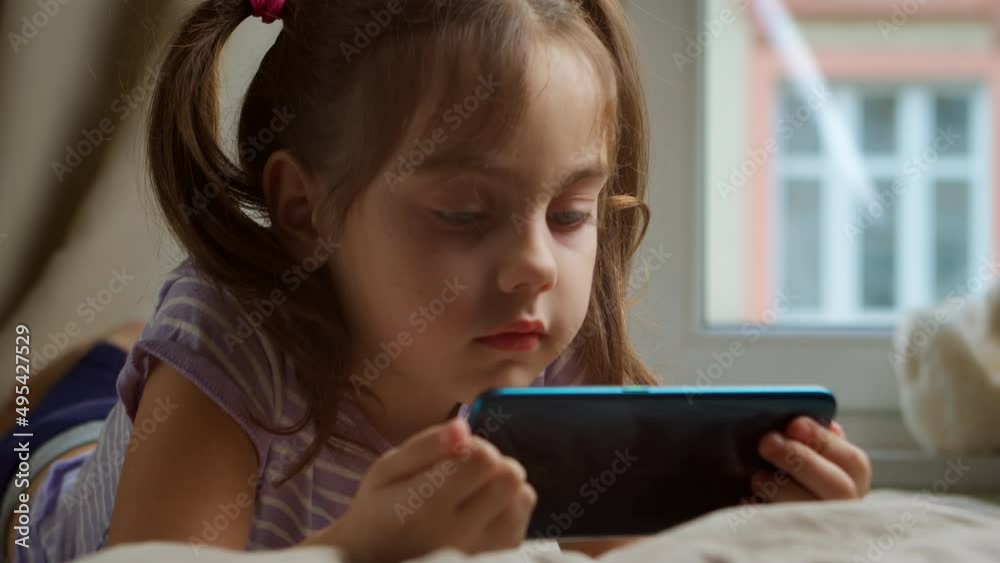 Little girl using a smartphone is watching the Internet in the bedroom. Little girl using a smartphone is watching the Internet in the bedroom.