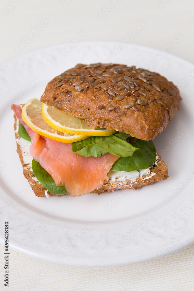 Closeup of homemade sandwich with slice of salmon, fresh lettuce leaf, cream cheese and lemon. Healthy food for family.