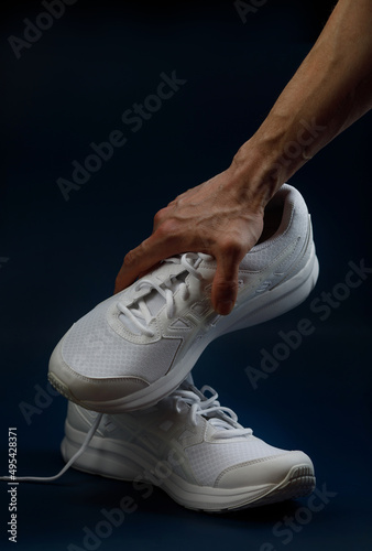 The male hand holds a white sneaker on a dark blue background. A couple of white sneakers.