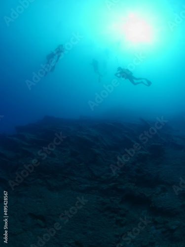 scuba divers under the boat coming up sun beam and sun ray on the surface underwater ocean scenery ascending descending