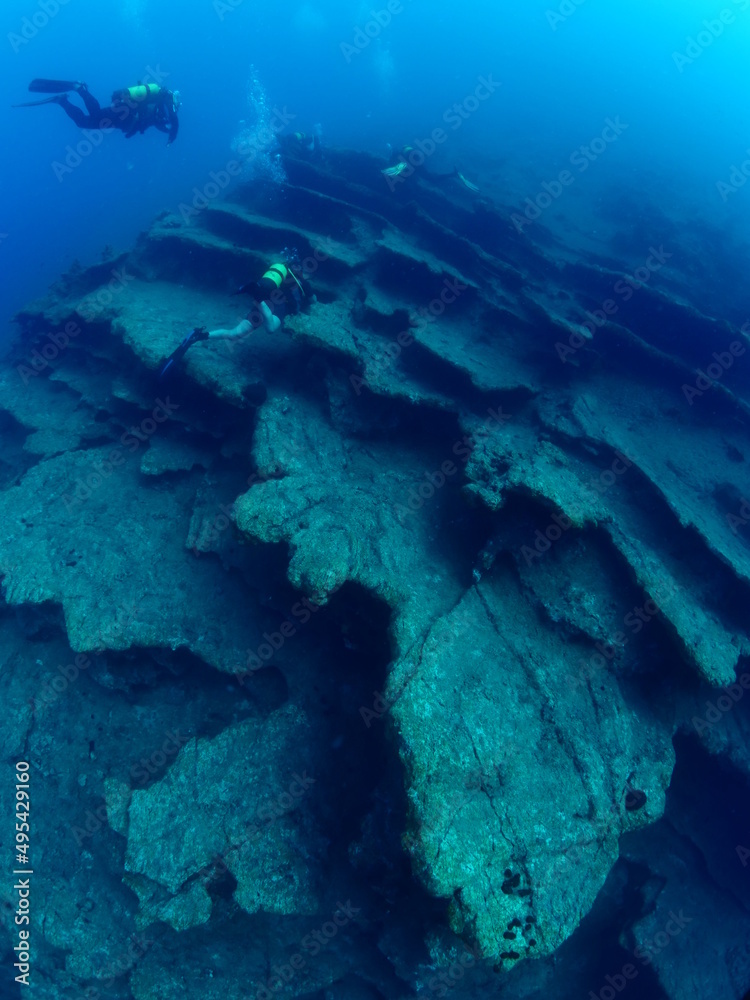 scuba divers around a reef underwater deep blue water big rock 