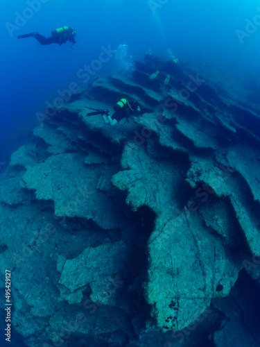 scuba divers around a reef underwater deep blue water big rock 
