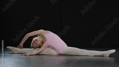 Teenager talented flexible professional acrobat ballerina dancer girl child sitting on floor on splits twine leaning to side stretching practicing acrobatic gymnastic elements training in dance class