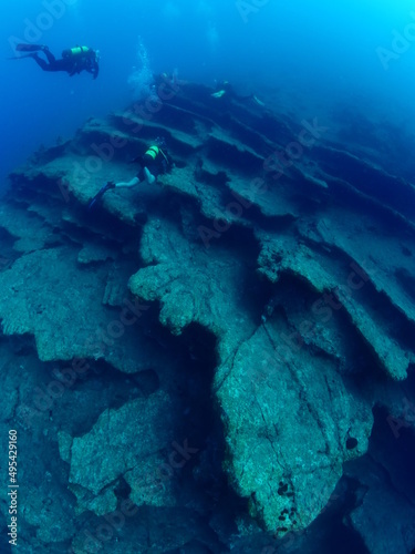 scuba divers around a reef underwater deep blue water big rock  © underocean