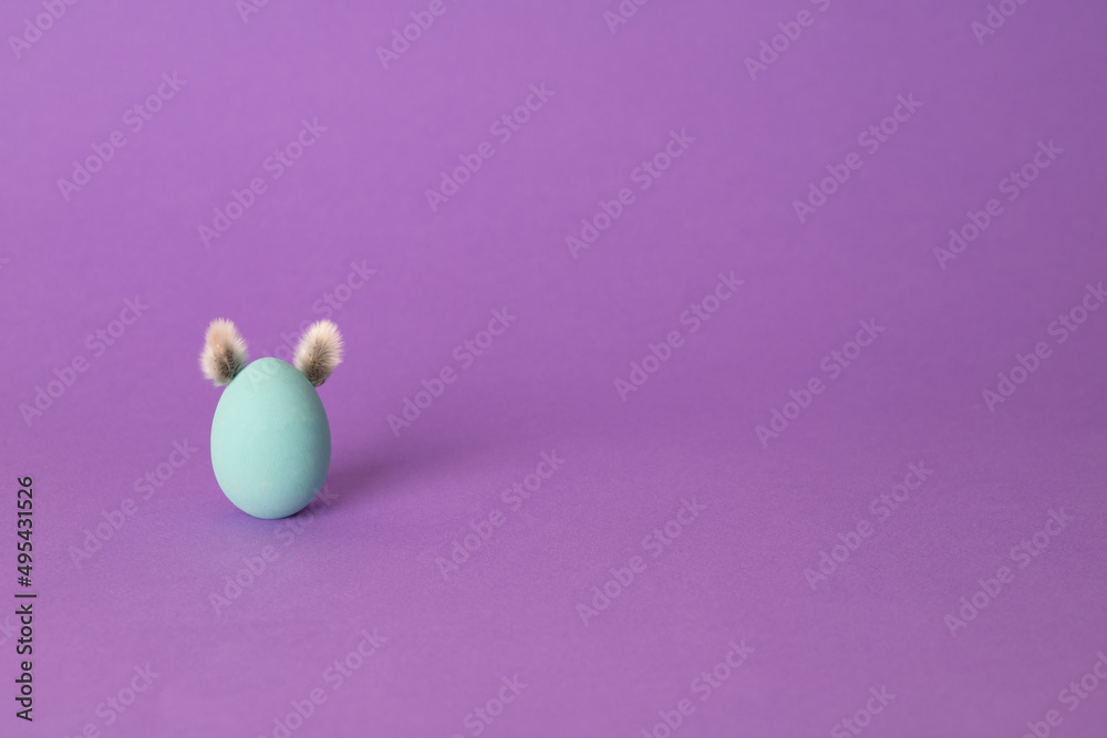 Row of colorful Easter eggs with willow bud ears painted in simple colors on a light purple background - side view with copy space