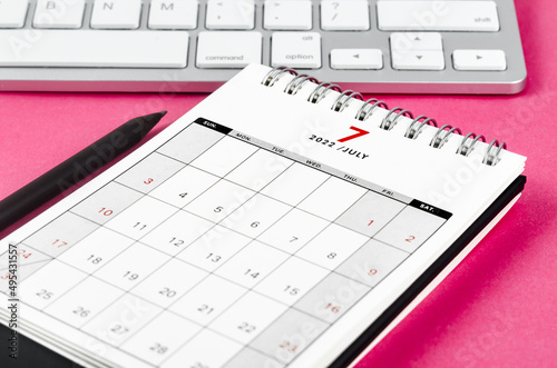 July 2022 desk calendar with pencil on pink background.
