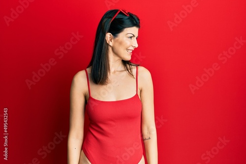 Young hispanic woman wearing swimsuit and sunglasses looking away to side with smile on face, natural expression. laughing confident.