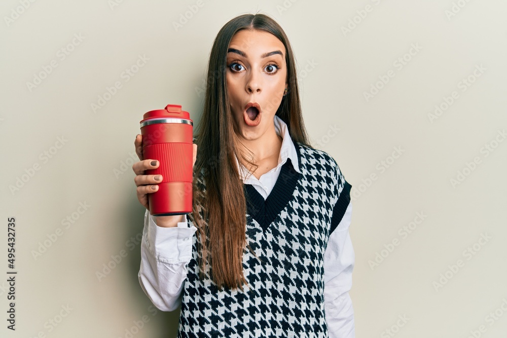 Beautiful brunette young woman drinking a take away cup of coffee scared and amazed with open mouth for surprise, disbelief face Beautiful brunette young woman drinking a take away cup of coffee scared and amazed with open mouth for surprise, disbelief face