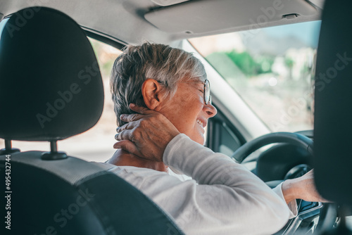 Rear view of old woman having neck pain while driving a car. One senior or mature people feeling bad for injury. photo