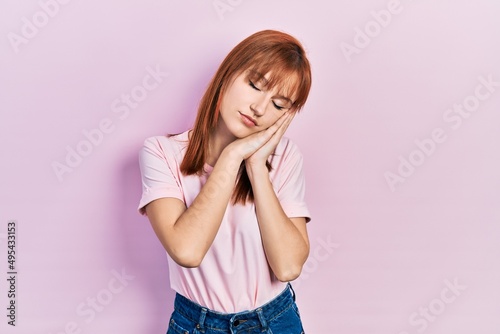 Redhead young woman wearing casual pink t shirt sleeping tired dreaming and posing with hands together while smiling with closed eyes.