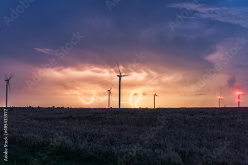 Photograph of large wind turbines in a row in the meadow during a lightning storm