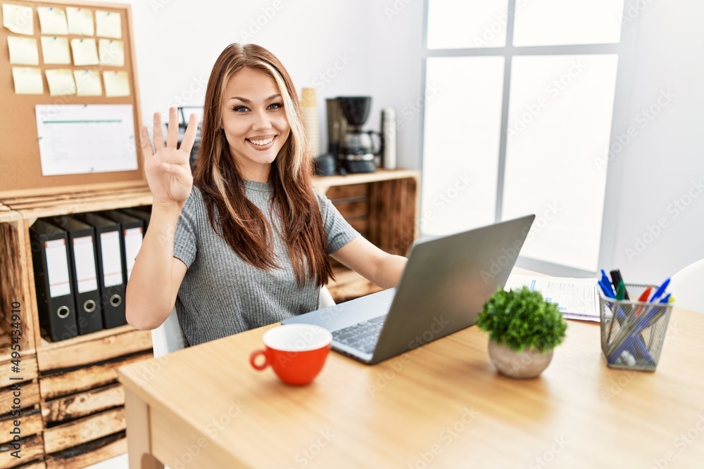 Young brunette woman working at the office with laptop showing and pointing up with fingers number four while smiling confident and happy. Young brunette woman working at the office with laptop showing and pointing up with fingers number four while smiling confident and happy.