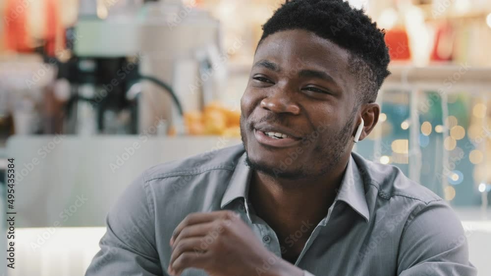 Close-up young happy african american man talking through wireless headphones smiling answering friendly business call communicating explaining chatting with friends remotely using modern technology