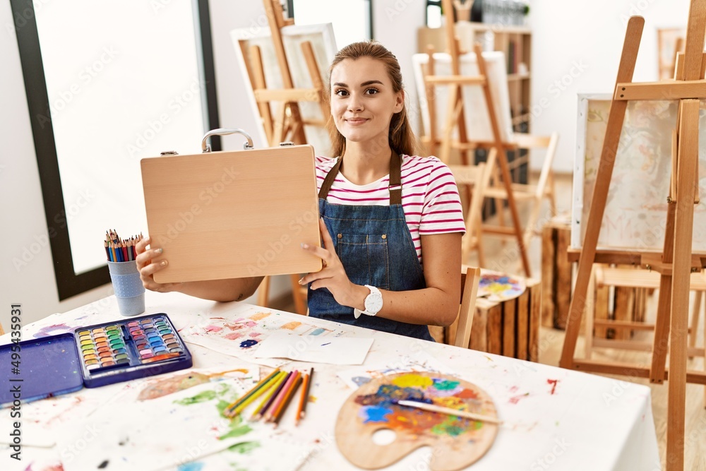 Young woman sitting on table holding draw suitcase at art studio