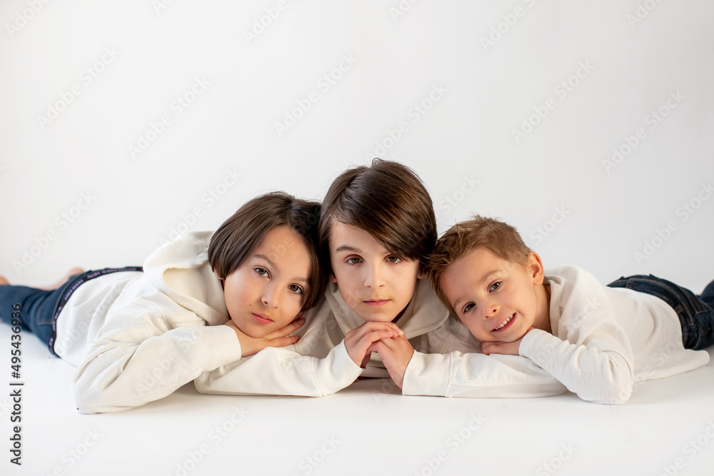Cute stylish toddler child and older brothers, boys with white shirts on white background, family kids portrait Cute stylish toddler child and older brothers, boys with white shirts on white background, family kids portrait