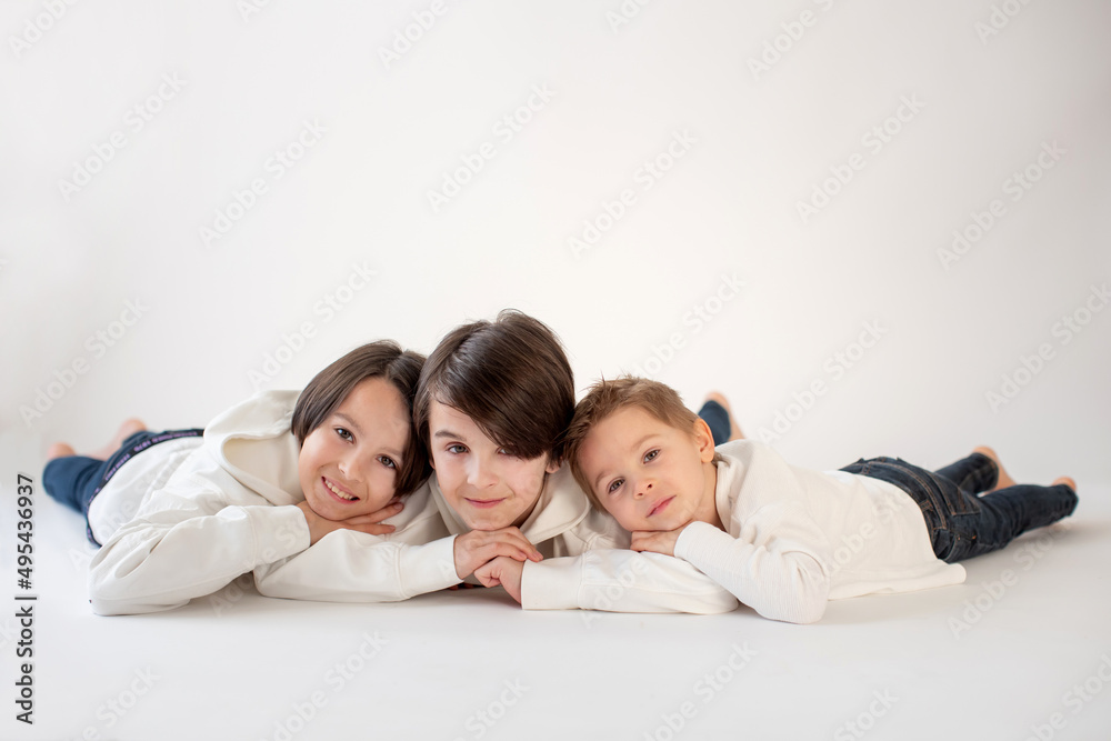 Cute stylish toddler child and older brothers, boys with white shirts on white background, family kids portrait Cute stylish toddler child and older brothers, boys with white shirts on white background, family kids portrait