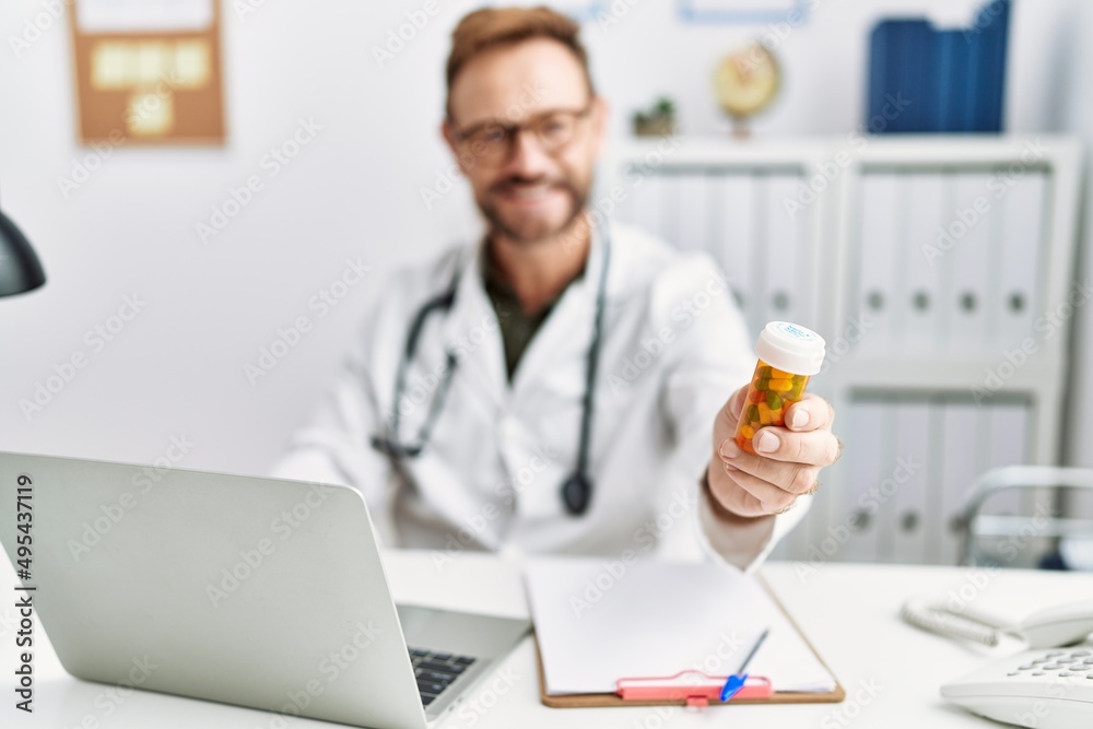 Middle age hispanic man wearing doctor uniform holding pills at clinic Middle age hispanic man wearing doctor uniform holding pills at clinic