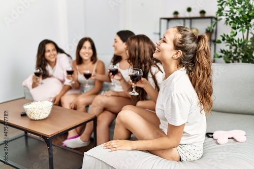 Group of young hispanic women celebrating pajamas party drinking red wine at home.