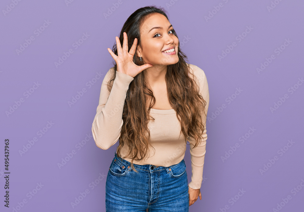 Young hispanic girl wearing casual clothes smiling with hand over ear listening an hearing to rumor or gossip. deafness concept. Young hispanic girl wearing casual clothes smiling with hand over ear listening an hearing to rumor or gossip. deafness concept.