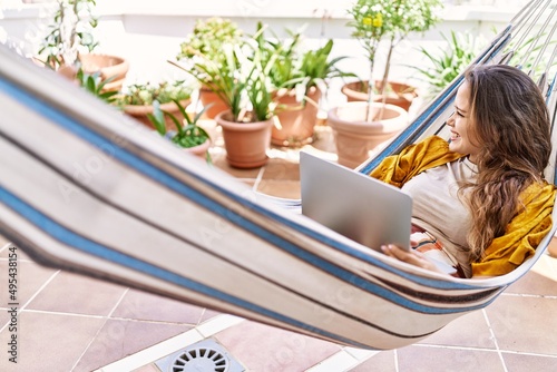 Young hispanic girl using laptop lying on hammock at the terrace.