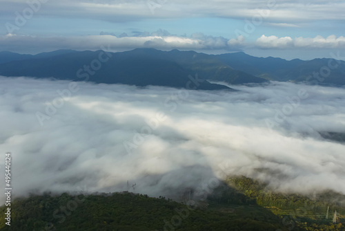 The mountain lowland is covered with fog. In the background are mountain ranges, sky and rain clouds. Beautiful landscape with fog.