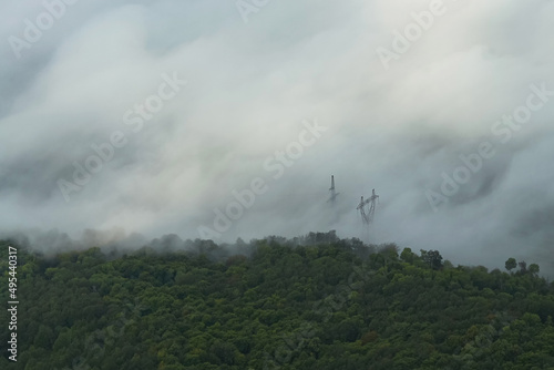 The view from the top of the green forest is obscured by mist. Through the fog you can see the poles of the power lines. It's a beautiful landscape.