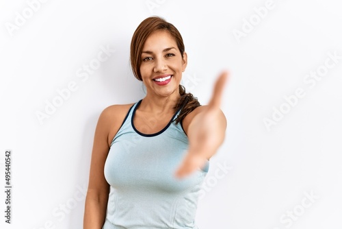 Young latin woman wearing sporty clothes over isolated background smiling friendly offering handshake as greeting and welcoming. successful business.