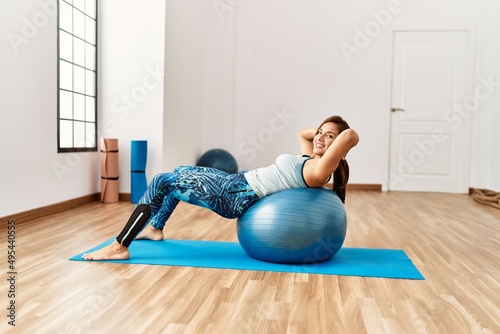 Young latin woman smiling confident training abs exercise using ball at sport center