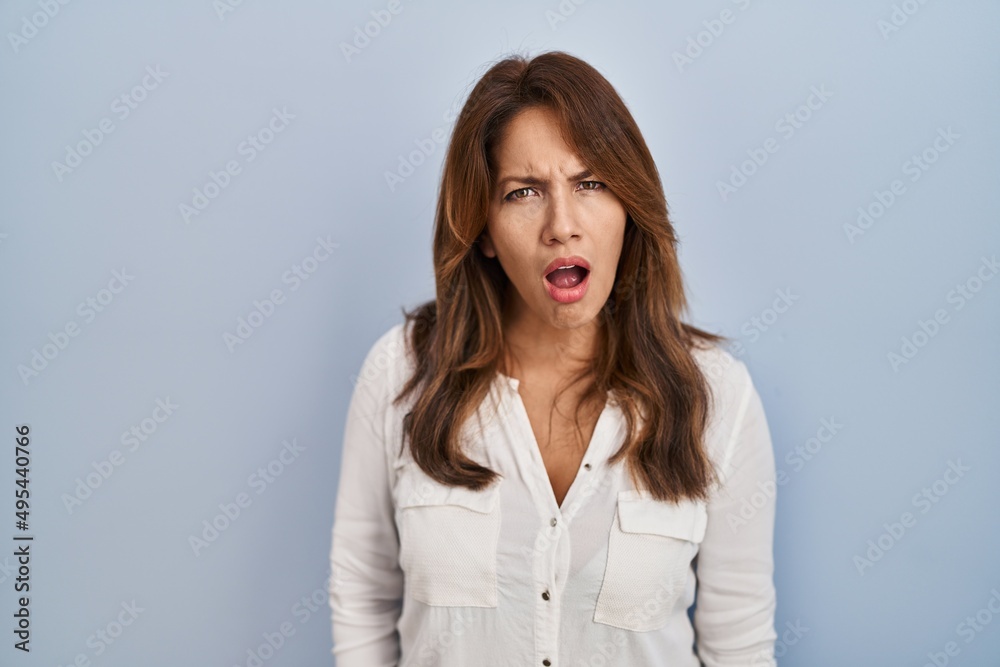 Hispanic woman standing over isolated background in shock face, looking skeptical and sarcastic, surprised with open mouth