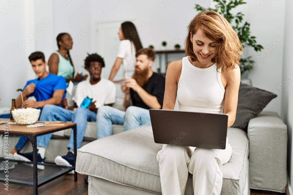 Group of young friends smiling happy sitting on the sofa. Woman using laptop at home. Group of young friends smiling happy sitting on the sofa. Woman using laptop at home.