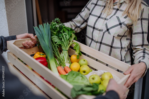 Man holding crate with vegetales and fruit and delivering it to woman standing at doorway. photo