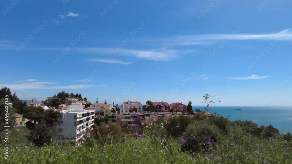 Driving on the road outside Castillo de Gibralfaro Castle. Beautiful view of the Mediterranean ocean from the top of the hill. Buildings below on the side of the road. Cars parked on the street. Driving on the road outside Castillo de Gibralfaro Castle. Beautiful view of the Mediterranean ocean from the top of the hill. Buildings below on the side of the road. Cars parked on the street.