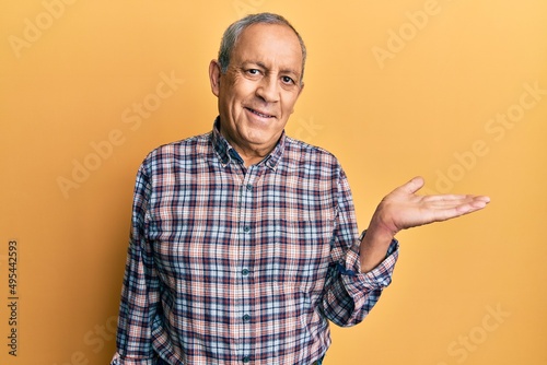 Handsome senior man with grey hair wearing casual shirt smiling cheerful presenting and pointing with palm of hand looking at the camera.