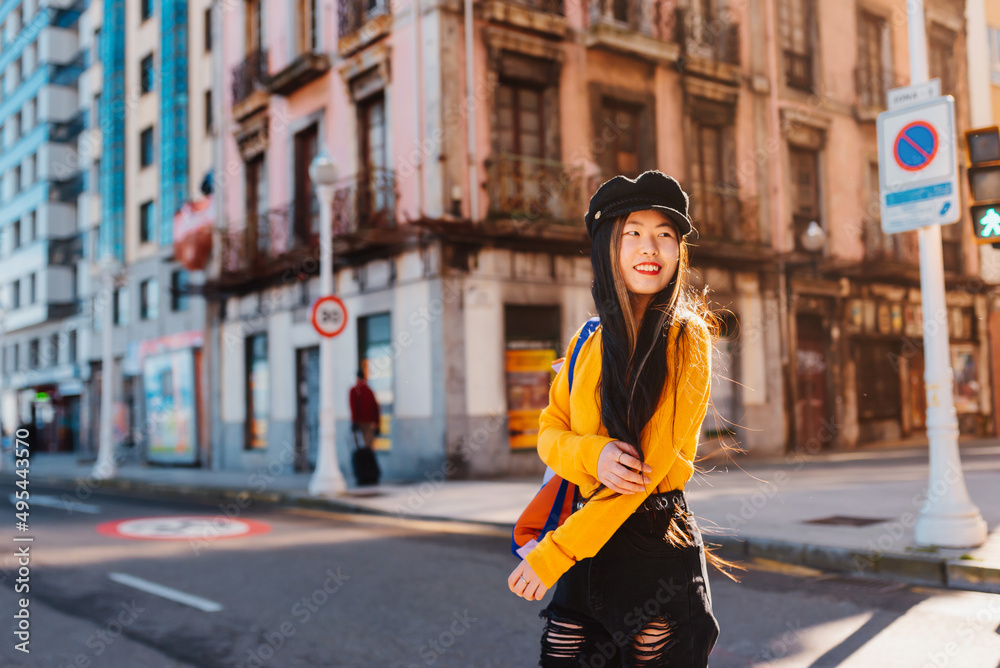 Asian young girl doing tourism in Europe. young chinese woman crossing a crosswalk in a city on a sunny day.